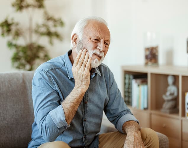 Older man holding his cheek in pain, needing an emergency dentist in Burke, VA